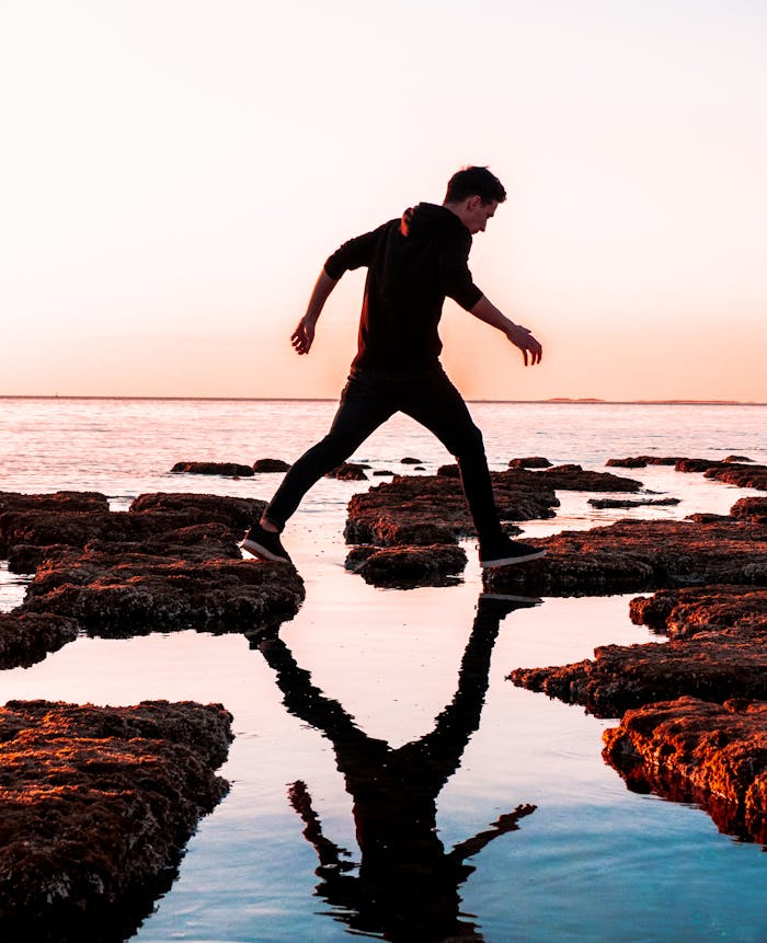 Silhouette of a man balancing on coastal rocks at sunrise in Peroj, Croatia.